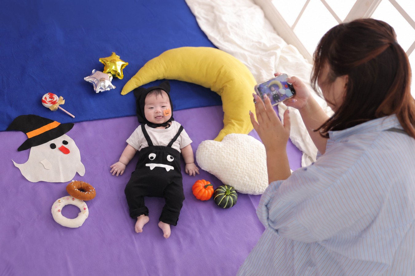 ハロウィンのセットで寝ている赤ちゃんを、ママがスマホで撮影している様子